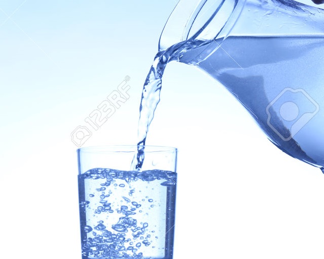 Pour water from  pitcher into  glass, on dark blue background